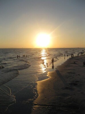 A beach at sunset with people walking along the shore.