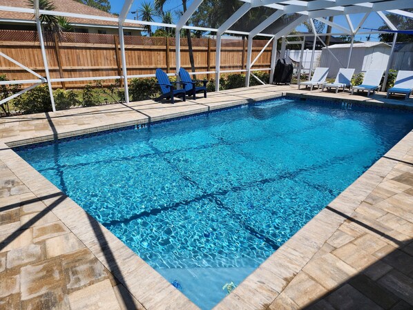 A rectangular swimming pool with clear blue water, surrounded by stone tiles.