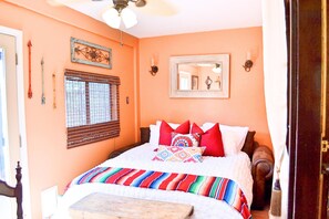 A bedroom with a bed, a window with blinds, a ceiling fan, a mirror, and a door.