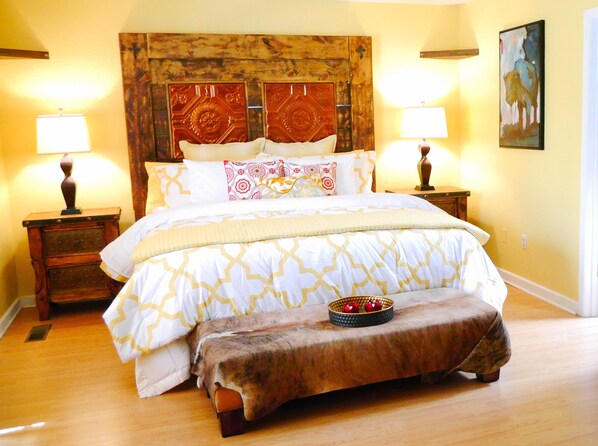 A bedroom with a large bed, two bedside tables, a headboard with intricate designs, and a painting on the wall.