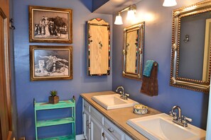 A bathroom with two sinks, a mirror, and framed pictures on the wall.