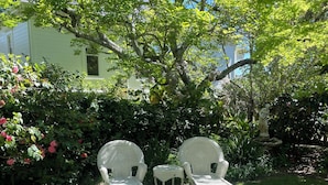 Two wicker chairs and a small table in a garden with a house in the background.
