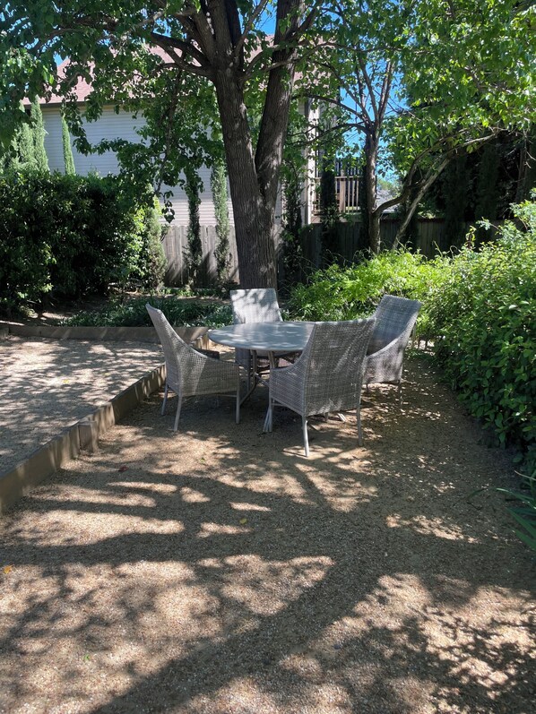 Un patio al aire libre con una mesa y cuatro sillas, rodeado de árboles y una valla de madera.