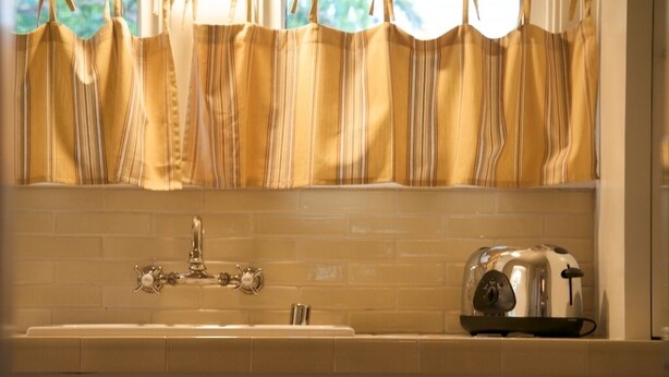 Una cocina con salpicadero de azulejos blancos, un tostador de acero inoxidable y una ventana con cortina a rayas.