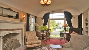Une pièce de style traditionnel avec une cheminée, deux fauteuils, une table avec une lampe et une vue dégagée sur l’extérieur grâce à de grandes fenêtres.
