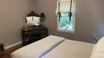 Quarto com cama, penteadeira, cadeira, janela com cortinas e abajur.
