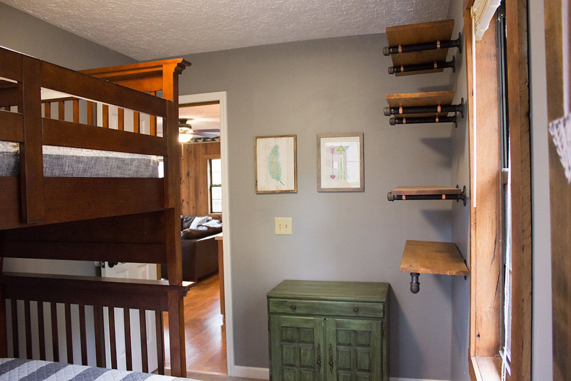 A room with a bunk bed, a green chest of drawers, and two framed pictures on the wall.