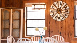 Un intérieur en bois avec une table à manger, des chaises blanches, une grande horloge et une fenêtre donnant sur un beau paysage.