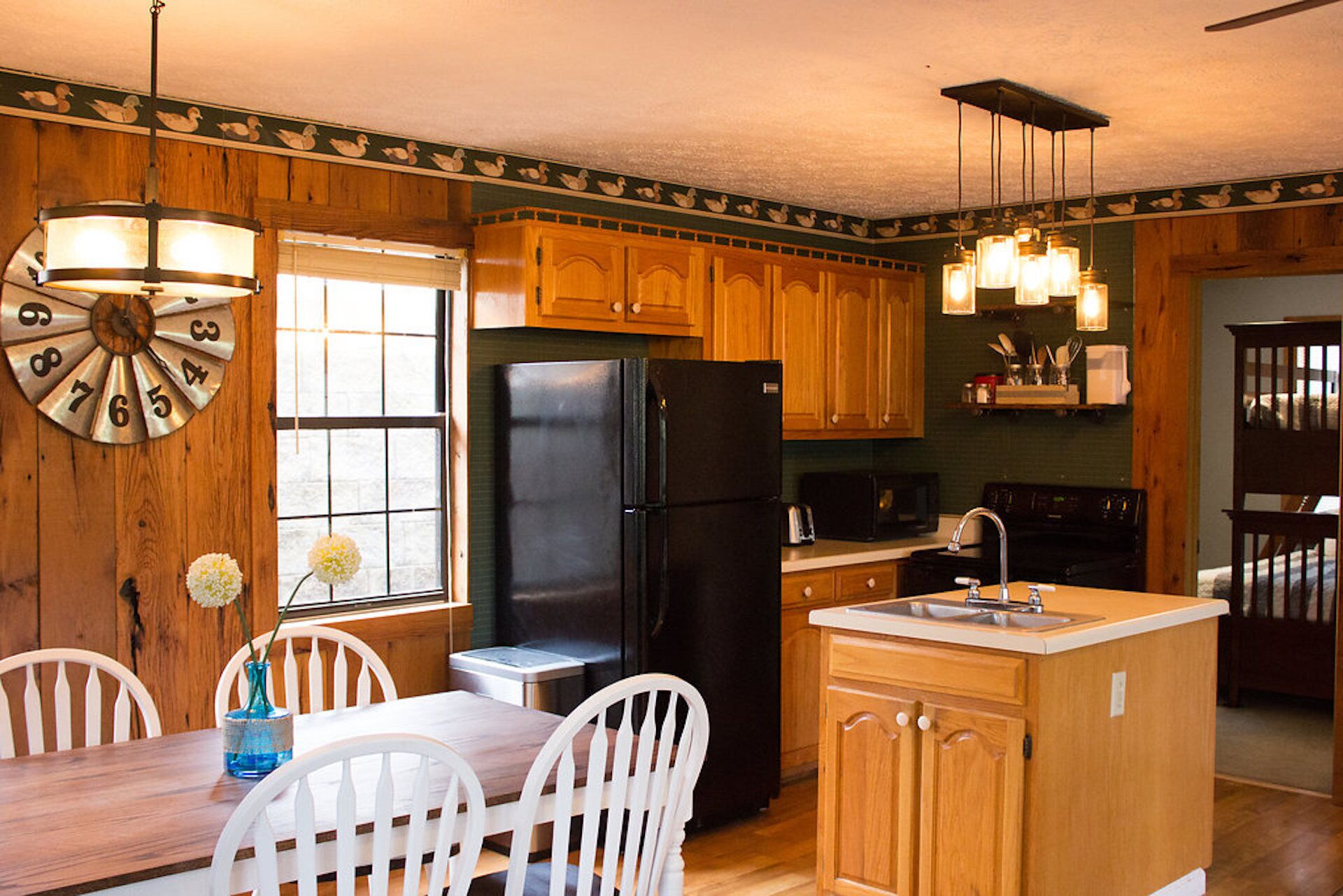 A kitchen with wooden cabinets, a black refrigerator, a dining table with chairs, and a small island with a sink.
