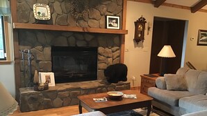 A cozy living room with a stone fireplace, a comfortable couch, and a wooden coffee table. - Enjoy Amazing Smoky Mountain View in Large, Comfortable Home in Treetops! (Franklin)