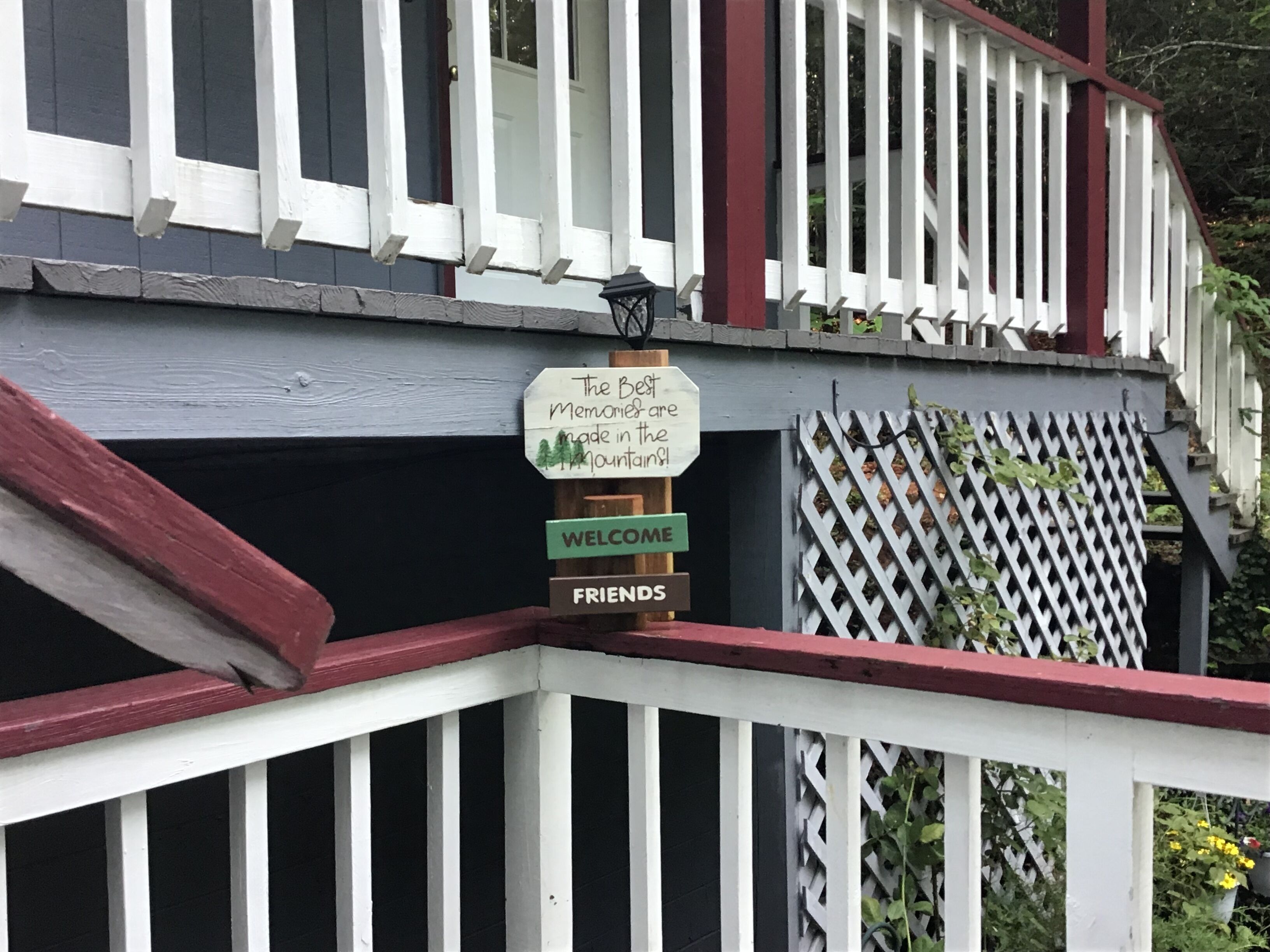 Eine Holzterrasse mit weißer Reling und einem Schild mit der Aufschrift 'The Best Memories are made in the Mountains!'