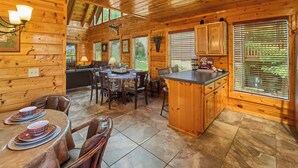 A wooden cabin interior with a dining area, kitchen, and large windows. - Near Dollywood/5/3/Mtn Views/ Fast Wifi/Arcade/Theater Rm/Hot Tub/Billiards (Sevierville)