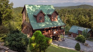A large log cabin with a green roof, a porch, and a small adjacent building. - Near Dollywood/5/3/Mtn Views/ Fast Wifi/Arcade/Theater Rm/Hot Tub/Billiards (Sevierville)