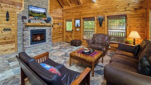 A log cabin interior with a stone fireplace, leather furniture, and wooden beams. - Near Dollywood/5/3/Mtn Views/ Fast Wifi/Arcade/Theater Rm/Hot Tub/Billiards (Sevierville)