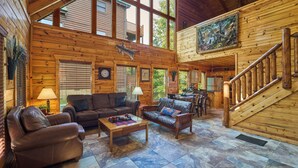 A spacious log cabin interior with a large living area, wooden walls, and a staircase leading to an upper level. - Near Dollywood/5/3/Mtn Views/ Fast Wifi/Arcade/Theater Rm/Hot Tub/Billiards (Sevierville)