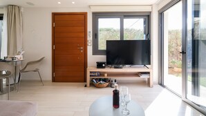 Ein modernes Wohnzimmer mit Flachbildfernseher, einer Holztür, einem Essbereich mit Tisch und Stühlen und einem großen Fenster mit Blick ins Freie.