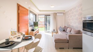 Ein modernes Wohnzimmer mit einer Couch, einem Essbereich mit Tisch und Stühlen, einer Küche mit Herd und einer Schiebeglastür, die zu einem Außenbereich führt.