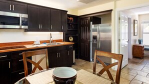 Una cocina moderna con armarios oscuros, electrodomésticos de acero inoxidable y un comedor con mesa y sillas.