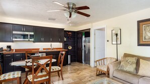 Una cocina moderna con armarios oscuros, un comedor con sillas de madera, una mesa de centro de vidrio y un ventilador de techo.