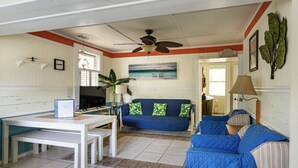 A room with a white ceiling fan, a blue sofa with green cushions, a white table with benches, and a large plant. - Lighthouse Cottage--1.5 blocks from beach.  (Tybee Island)
