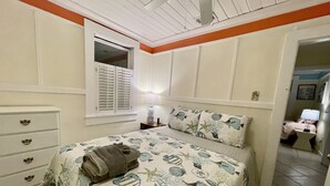 A bedroom with a bed, a nightstand, a dresser, a window with shutters, and a door leading to another room. - Lighthouse Cottage--1.5 blocks from beach.  (Tybee Island)