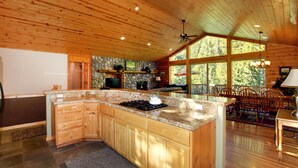 A spacious kitchen with a large island, wooden ceiling, stone wall, and large windows. - At Home in the Mountains , 7 bdrms 5 baths, Hot tub, Sauna, Steam rm & more (South Lake Tahoe)