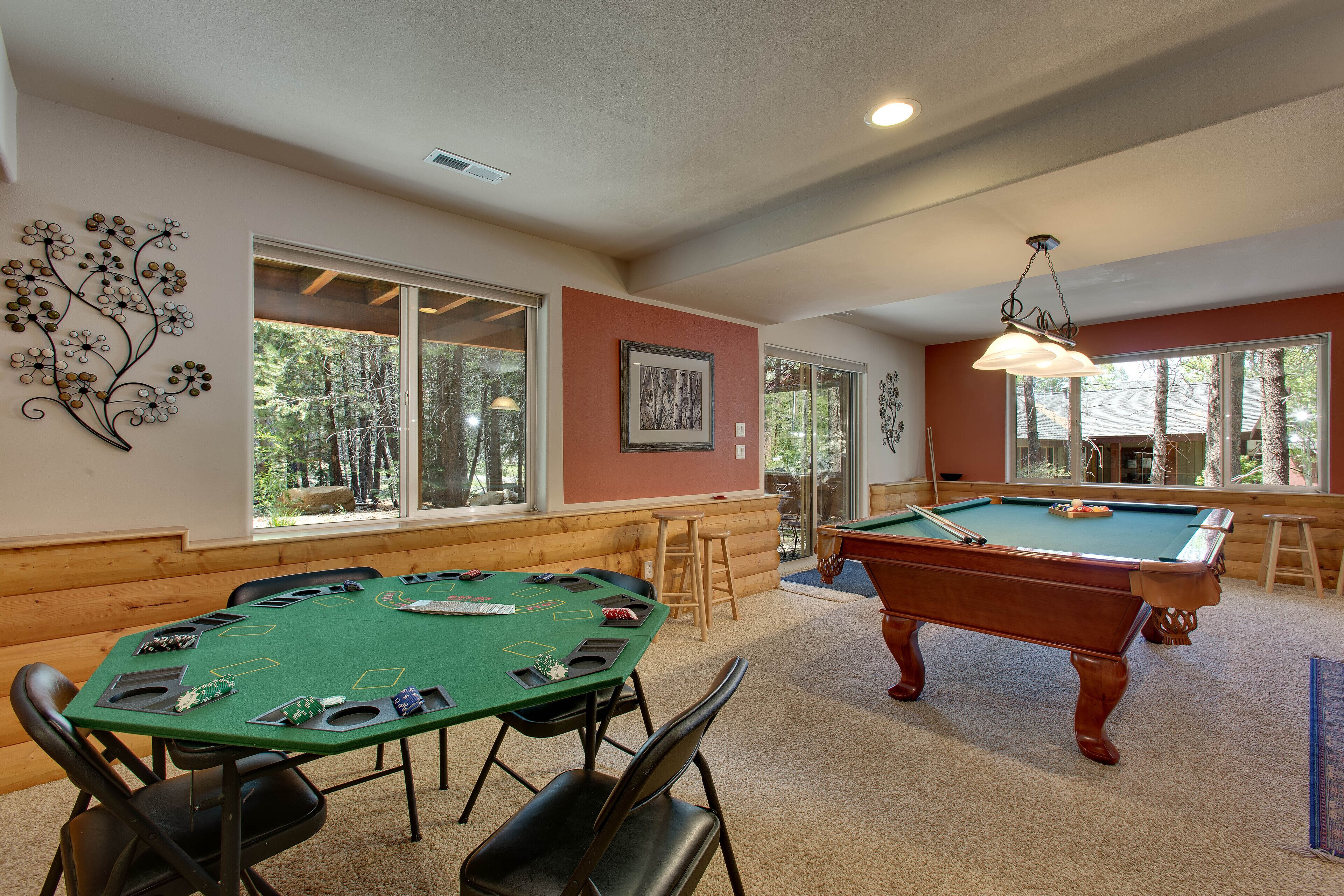 A pool table in a room with large windows, a green felt table, and pool cues.