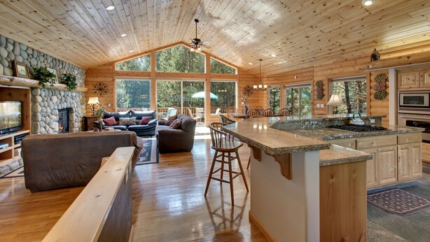 A spacious log cabin interior with a large living area, a kitchen with granite countertops, and a stone fireplace. - At Home in the Mountains , 7 bdrms 5 baths, Hot tub, Sauna, Steam rm & more (South Lake Tahoe)