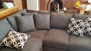 A sectional sofa with patterned cushions in a living room with a brick fireplace and a wooden table with yellow items. - COZY 2 BEDROOM OCEAN VIEW las gaviotas  17#2 (rosarito beach)