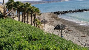 A coastal landscape with a rocky beach, palm trees, and a view of the sea and distant hills. - COZY 2 BEDROOM OCEAN VIEW las gaviotas  17#2 (rosarito beach)