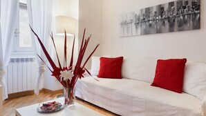 A white sofa with red cushions, a vase with red and white flowers, and a cityscape painting on the wall. - Fontana di Trevi and Spanish Steps. Modern and elegant (Roma)