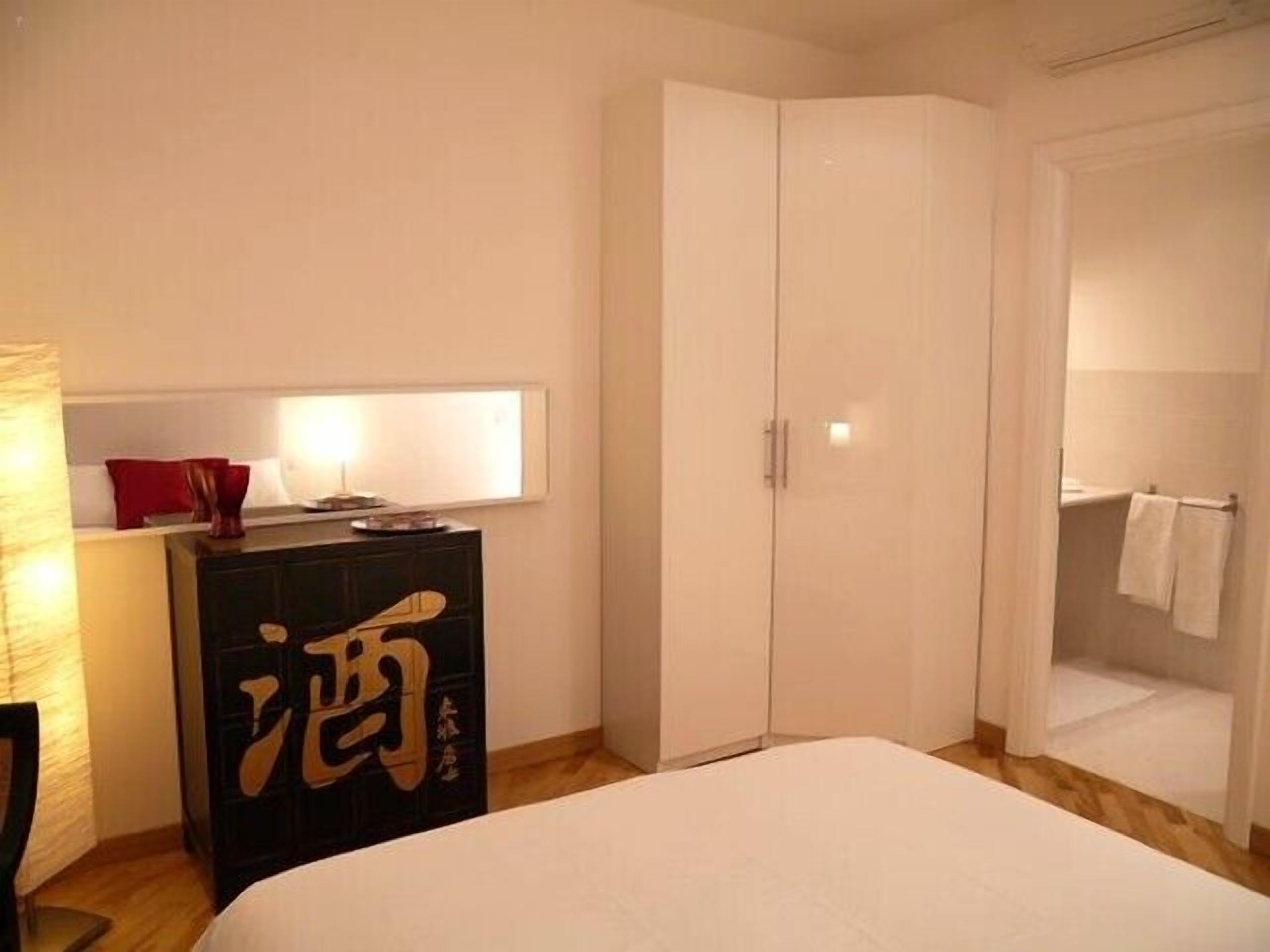 Ein Schlafzimmer mit Bett, Kleiderschrank, Schreibtisch und Lampe sowie einem Fenster.