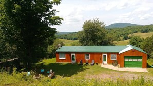 A rustic wooden house with a green roof, a garage, and a lawn with outdoor seating. - Mountain Top Retreat, 116 private acres (Hobart)