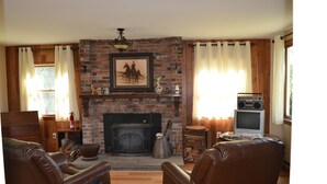 A living room with a brick fireplace, leather chairs, a television, and a bookshelf. - Mountain Top Retreat, 116 private acres (Hobart)