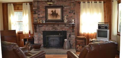 Una sala de estar con chimenea de ladrillo, sillones de cuero, un televisor y una estantería.