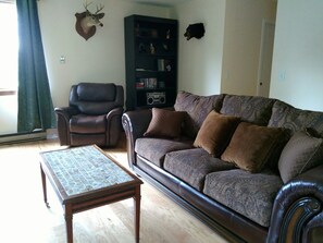 Una sala de estar con un sofá de cuero, un sillón a juego, una mesa de centro, una estantería y cabezas de animales montadas en la pared.