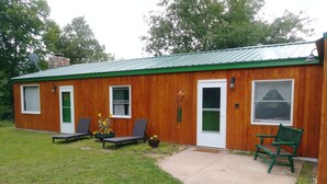 A wooden building with a green roof, a welcome sign, and two lounge chairs with potted sunflowers. - Mountain Top Retreat, 116 private acres (Hobart)