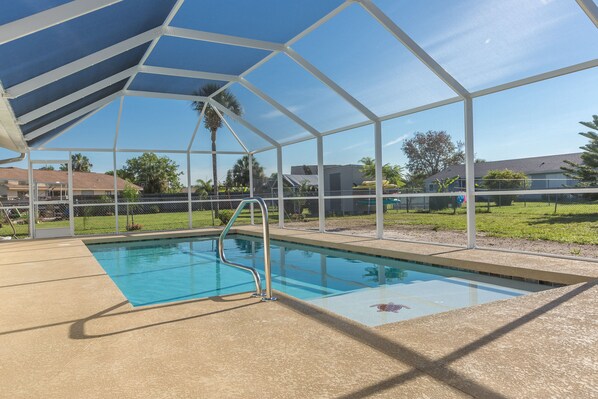 Una piscina techada con una escalera de metal, rodeada por una valla y palmeras.