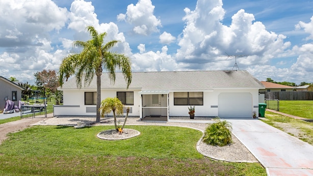 A single-story house with a covered porch, a garage, and a small lawn with a palm tree.