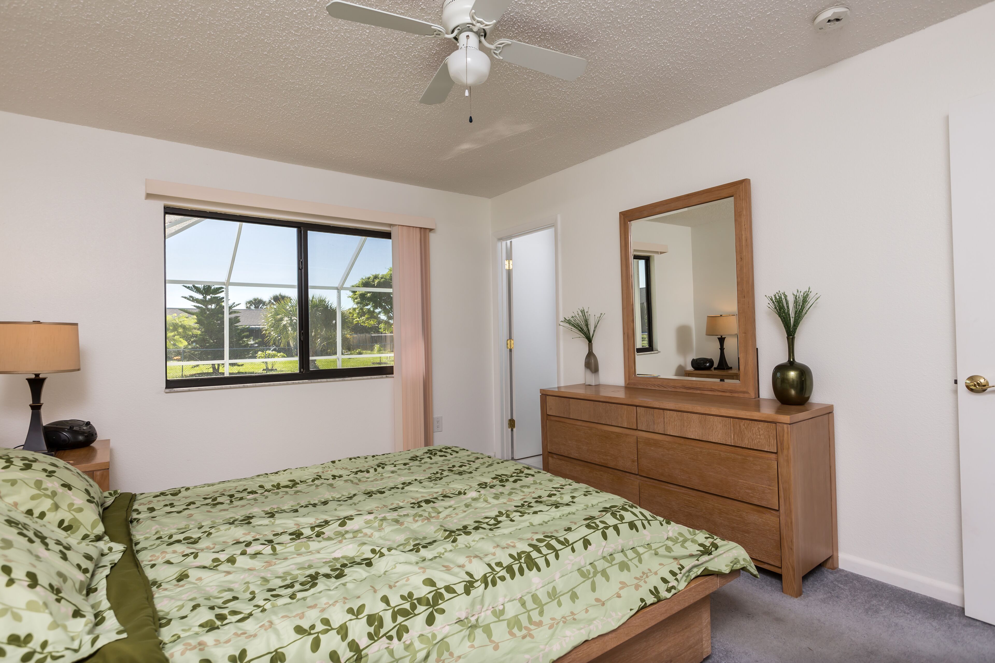 Ein Schlafzimmer mit einem Bett, einem Schminktisch, einem Spiegel, einem Fenster und einem Deckenventilator.