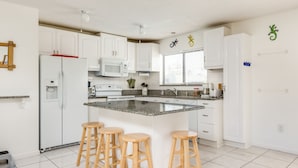 A modern kitchen with white cabinets, a granite countertop, a built-in microwave, a coffee maker, and three wooden stools.