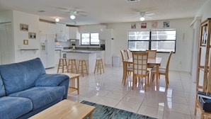 A modern kitchen with white cabinets, a refrigerator, and a microwave. There is a dining area with a table and chairs.