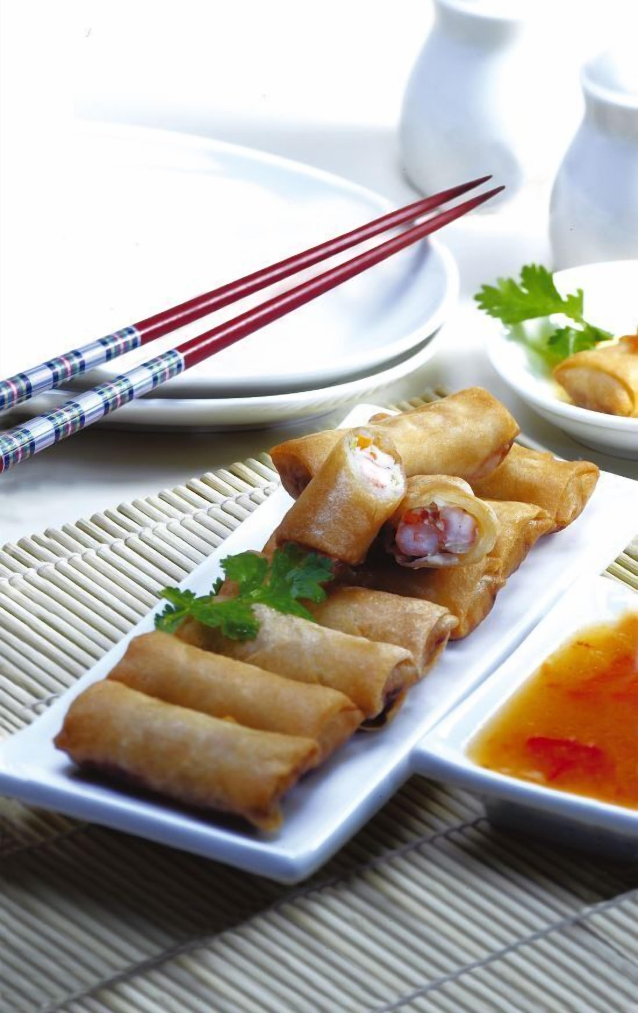 A plate of spring rolls with chopsticks and a small bowl of sauce.