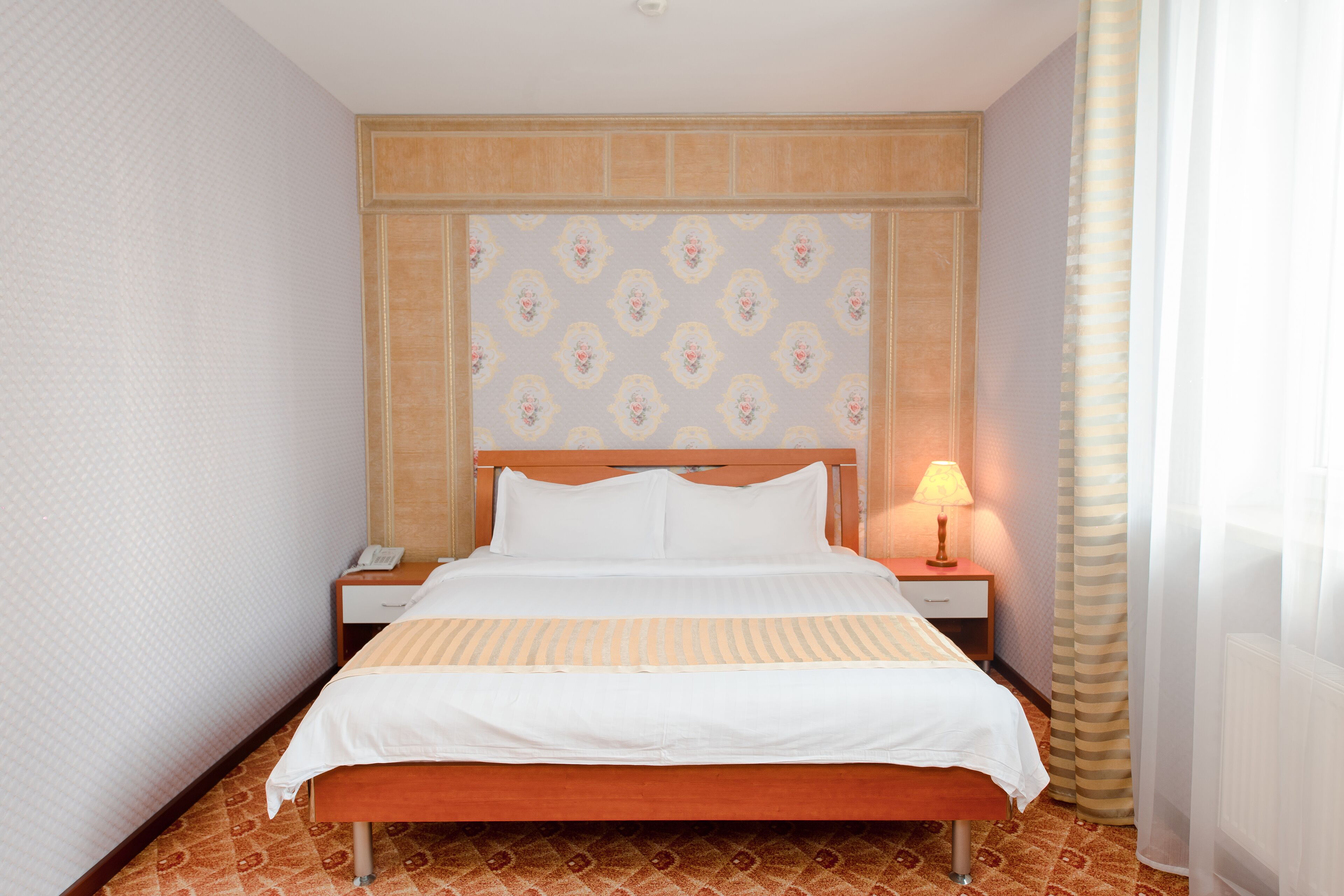A hotel room with a bed, a nightstand, a lamp, and a patterned carpet.