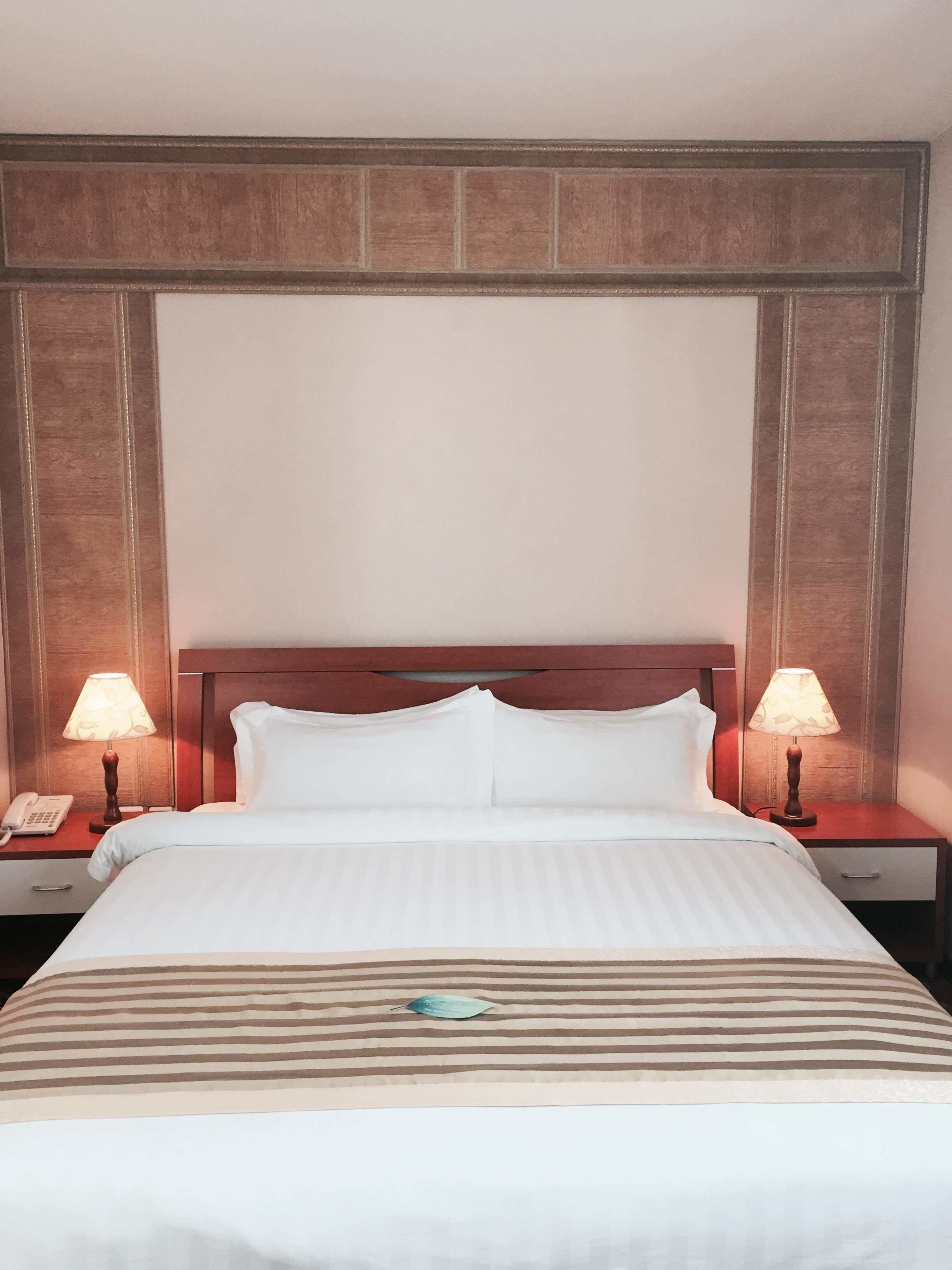 Una habitación de hotel con una cama, dos mesitas de noche, un teléfono y dos lámparas.
