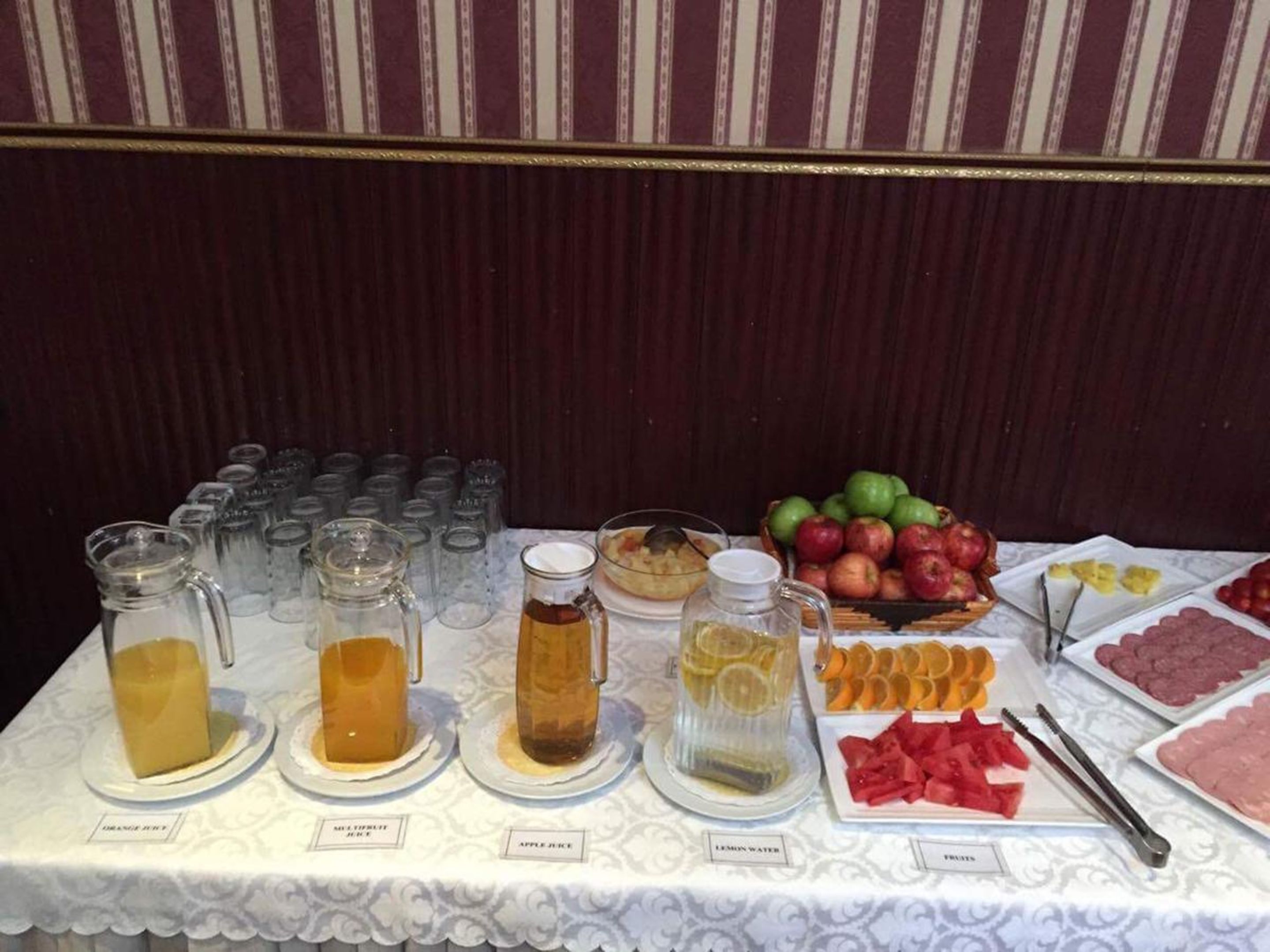 A buffet table with various food and drink options including juices, fruits, and a pie.