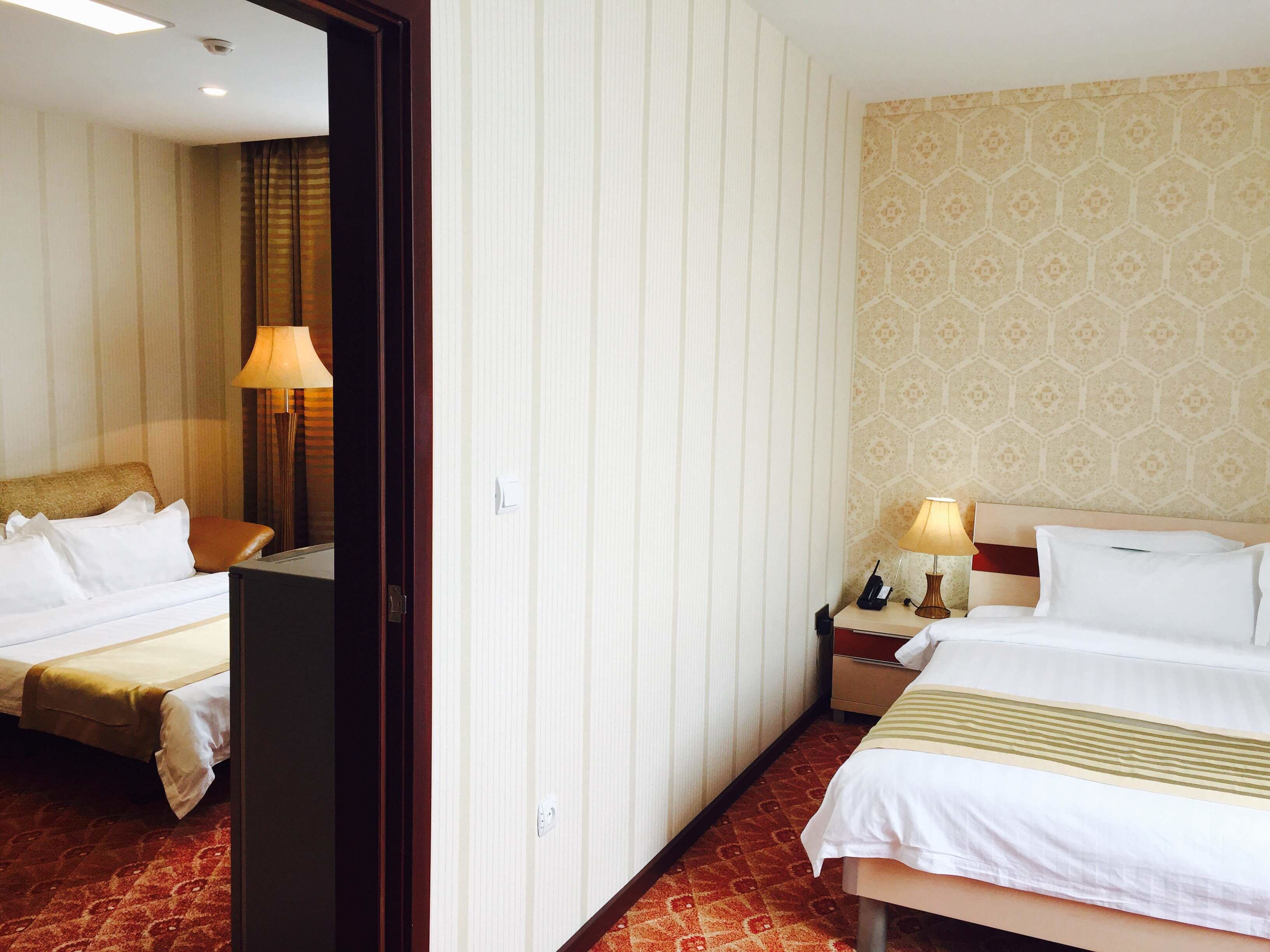Een hotelkamer met twee bedden, een nachtkastje met een lamp en een behangen wand.