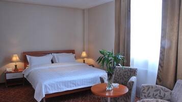 Habitación de hotel con una cama, dos lámparas de noche, una mesita de noche, una pequeña mesa con un florero y una silla.