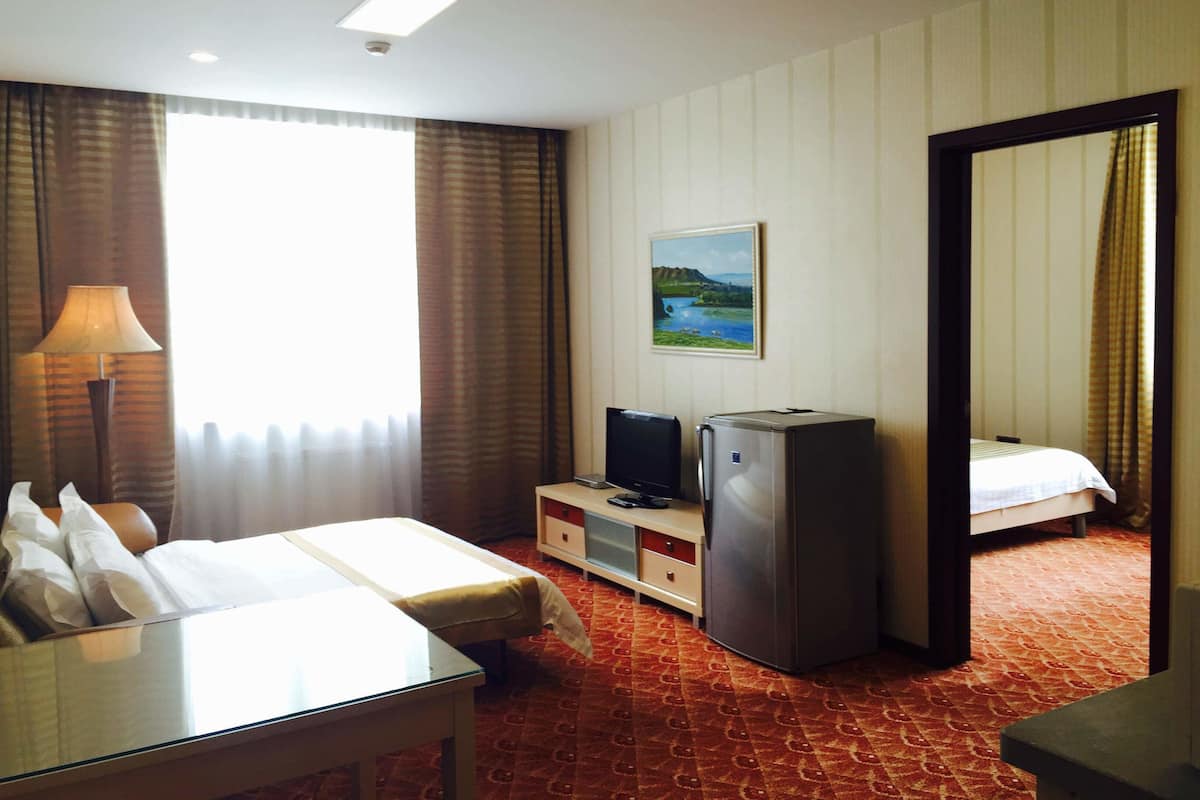 Et hotelværelse med en seng, et skrivebord, et fjernsyn, et køleskab og et billede på væggen.