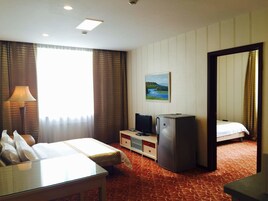 Quarto de hotel com uma cama, escrivaninha, televisão, frigorífico e um quadro na parede.